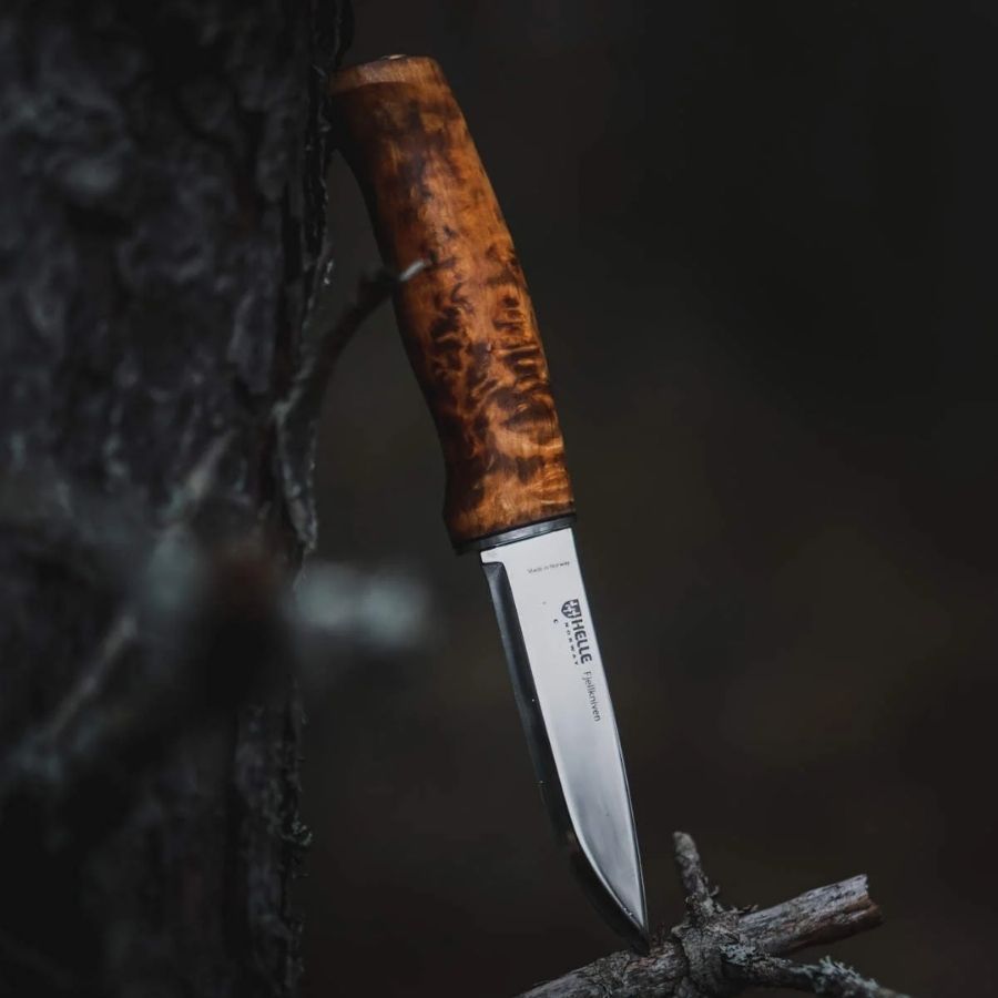 Helle Fjellkniven 12C27 bushcraft knife resting on a moss-covered log in a forest, highlighting its natural wood handle and sharp Scandinavian blade.