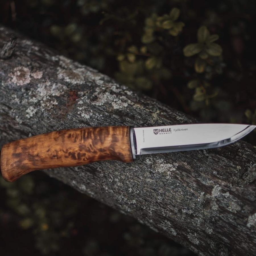 Helle Fjellkniven 12C27 bushcraft knife resting on a moss-covered log in a forest, highlighting its natural wood handle and sharp Scandinavian blade.