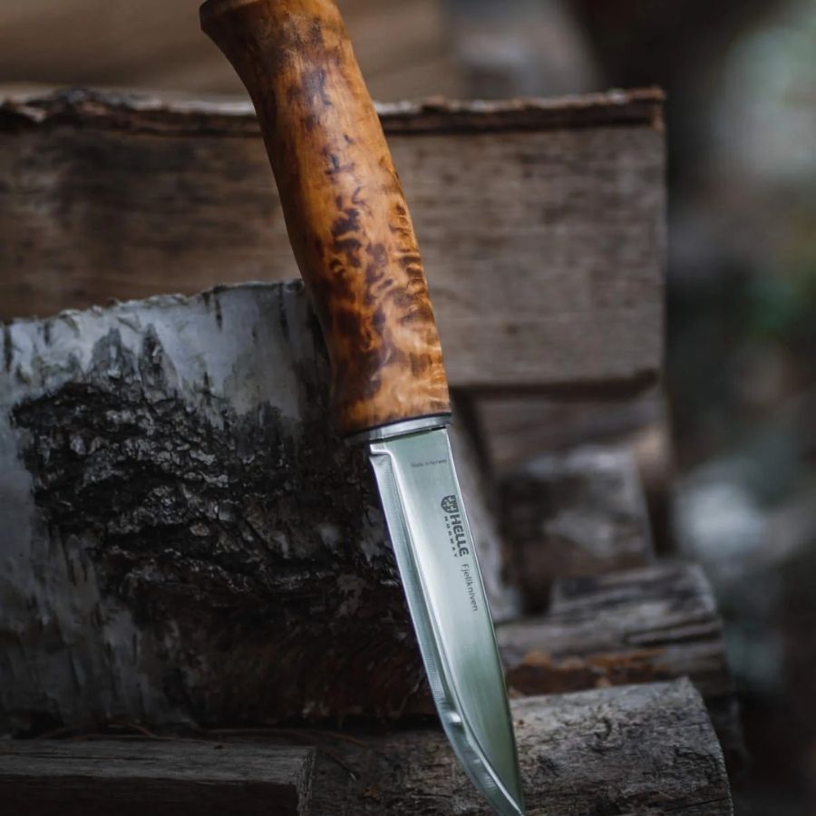Helle Fjellkniven 12C27 bushcraft knife resting on a moss-covered log in a forest, highlighting its natural wood handle and sharp Scandinavian blade.